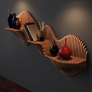 Op de afbeelding: Een wandplank van hout met een reeks verticale latten in een golvende structuur. De plank bevat drie glazen flessen, een notitieboek, een geurstokjesdiffuser en twee extra decoratieve glazen vazen in de kleuren zwart en rood.