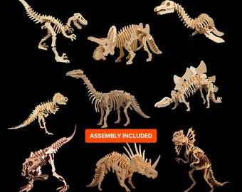 May include: A collection of eight light-colored wooden dinosaur skeleton models in various poses. Each figure is constructed from interlocking flat pieces. An orange rectangular label in the center displays the text ASSEMBLY INCLUDED.