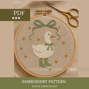 Pode incluir: Padrão de bordado com um pato branco com botas e laço verdes, rodeado por detalhes florais. O design está dentro de um bastidor de madeira, com uma tesoura dourada por perto. O texto "WHITE EMBROIDERY" é visível.