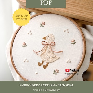 May include: An embroidered goose design in a wooden hoop. The goose is cream-coloured with a brown beak and feet, and a pink bow. The design includes small pink flowers and white dots. Text on the image says "Embroidery Pattern + Tutorial".