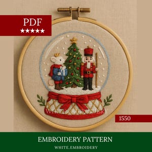 May include: Embroidered Christmas snow globe design in a wooden hoop. The design features a mouse, a nutcracker, and a Christmas tree. The base is red with a bow. The text "WHITE.EMBROIDERY" is visible.