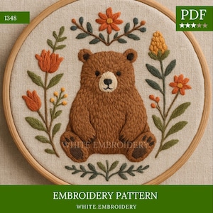 Puede incluir: Patrón de bordado con un oso marrón rodeado de flores naranjas y hojas verdes, dentro de un aro de madera. El diseño incluye el texto "EMBROIDERY PATTERN" y "WHITE.EMBROIDERY". El icono PDF es visible en la esquina superior derecha.