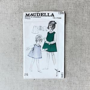 May include: A vintage Maudella sewing pattern envelope for a blouse and overdress, model 1391, for 3 and 4 years. The white paper envelope features black text and a black and white illustration of two children wearing the garments, one in a striped dress.