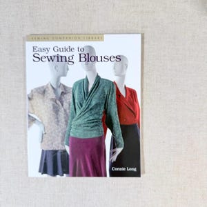 May include: A book titled "Easy Guide to Sewing Blouses" with images of blouses on mannequins. The cover features the text "Sewing Companion Library" and the author's name, Connie Long. The blouses are in shades of green, red, and beige.