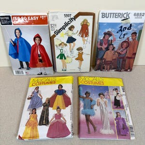 May include: Five vintage sewing pattern envelopes for costumes, including Simplicity S0702 with capes, Simplicity 5597 with cheerleader and school outfits, Butterick 6852 with historical attire, and two McCall's Costumes patterns featuring various dress designs.