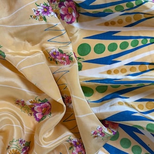 May include: A fabric featuring a light yellow background with a pattern of small pink and purple floral clusters. The design includes white diagonal lines and a section with blue pointed shapes interspersed with rows of green and yellow dots.