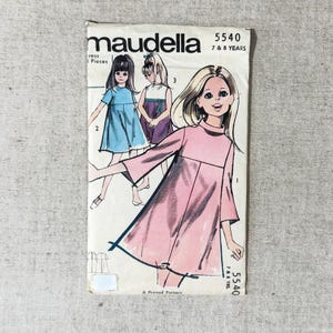 May include: A Maudella 5540 sewing pattern envelope for a dress in sizes 7 & 8 years. The front features illustrations of three children wearing different versions of the dress in pink, blue, and purple, with a high neckline and flared sleeves.