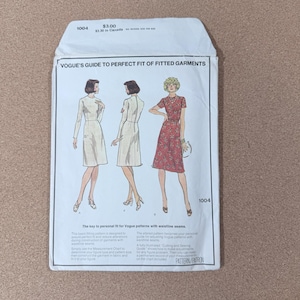 May include: A vintage Vogue sewing pattern envelope, featuring illustrations of three women in dresses. The envelope is white with text and the number 1004. The text reads "Vogue's Guide to Perfect Fit of Fitted Garments."