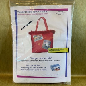 May include: A Frankie's Fabric Photo Printing kit in a clear plastic bag. The package features a red tote bag with fringe, two photo inserts, and text including 'Serger photo tote' and 'Kit # K203 Approximate finished size 12" x 14".'