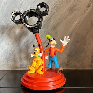 May include: A red and black Mickey Mouse themed desk organizer with a black metal Mickey Mouse head and a red base.  The organizer features a Goofy and Pluto figurine.