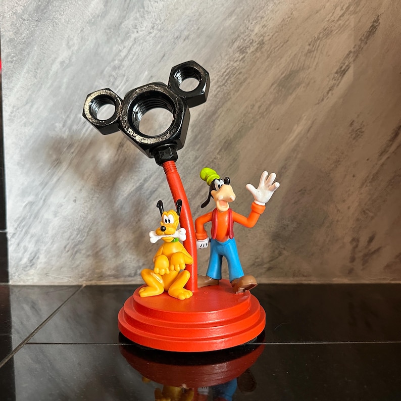 May include: A red and black Mickey Mouse themed desk organizer with a black metal Mickey Mouse head and a red base.  The organizer features a Goofy and Pluto figurine.