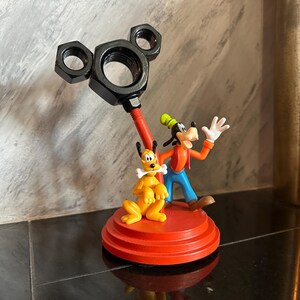 May include: A red and black Mickey Mouse themed figurine featuring Goofy and Pluto. Goofy is wearing a red shirt and blue pants. Pluto is holding a bone in his mouth. The figurine is made of plastic and is approximately 6 inches tall.