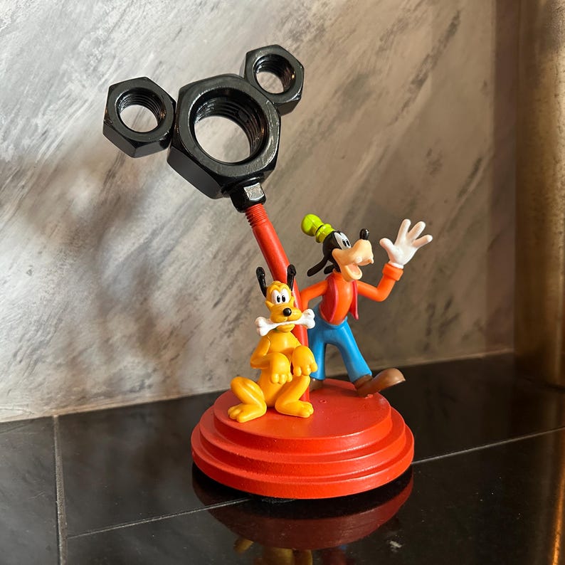 May include: A red and black Mickey Mouse themed figurine featuring Goofy and Pluto. Goofy is wearing a red shirt and blue pants. Pluto is holding a bone in his mouth. The figurine is made of plastic and is approximately 6 inches tall.