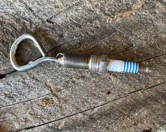 May include: A silver spark plug keychain with a blue and white spark plug attached to a silver ring.