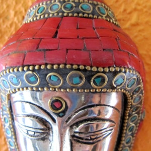 Op de afbeelding: Zilveren Boeddha-hoofd sculptuur met een rode koraal en turquoise moza&iuml;ek kroon. Het gezicht is gedetailleerd met een derde oog en een rode edelsteen.