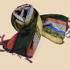 Op de afbeelding: Een kleurrijke zijden sjaal met een groen, rood, oranje, blauw en geel gestreept patroon. De sjaal heeft franjes aan de uiteinden en is versierd met kleine kralen.