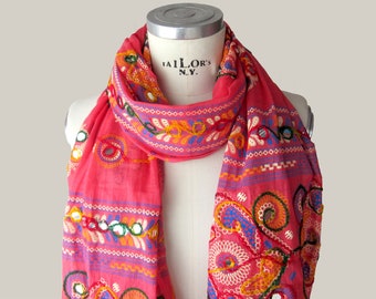 May include: A pink scarf with colorful embroidery and mirror accents. The scarf is draped over a mannequin's neck. The text "TAILOR'S N.Y." is visible on the mannequin's chest.