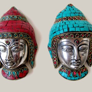 Op de afbeelding: Twee zilveren Boeddha-wandmaskers met ingewikkelde moza&iuml;ekontwerpen. Het ene masker heeft een rood moza&iuml;ekontwerp en het andere een turquoise moza&iuml;ekontwerp.