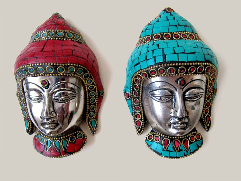 Op de afbeelding: Twee zilveren Boeddha-wandmaskers met ingewikkelde moza&iuml;ekontwerpen. Het ene masker heeft een rood moza&iuml;ekontwerp en het andere een turquoise moza&iuml;ekontwerp.