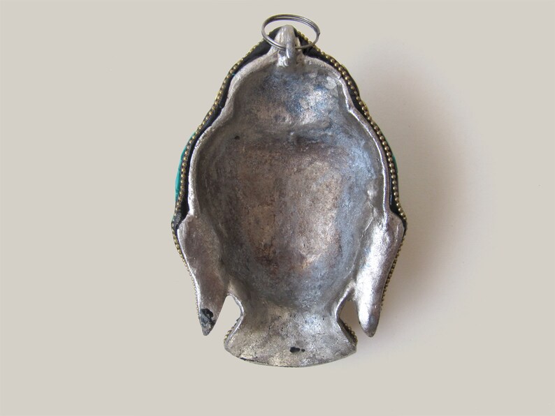 Op de afbeelding: Zilverkleurig metalen hanger met een Boeddha-gezichtsontwerp. De hanger heeft een groene steeninleg en goudkleurige accenten.