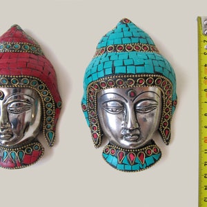 Op de afbeelding: Twee zilveren Boeddha-wanddecoraties met turquoise en rode moza&iuml;ektegels. De Boeddha-gezichten zijn zilver met een gouden rand. De Boeddha links heeft rode moza&iuml;ektegels en de Boeddha rechts heeft turquoise moza&iuml;ektegels.