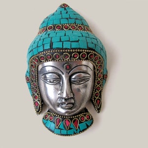 Op de afbeelding: Zilveren Boeddha-hoofd wanddecoratie met turquoise en rode moza&iuml;ekdetails. Het hoofd is omgeven door een decoratieve rand van turquoise en rode stenen.