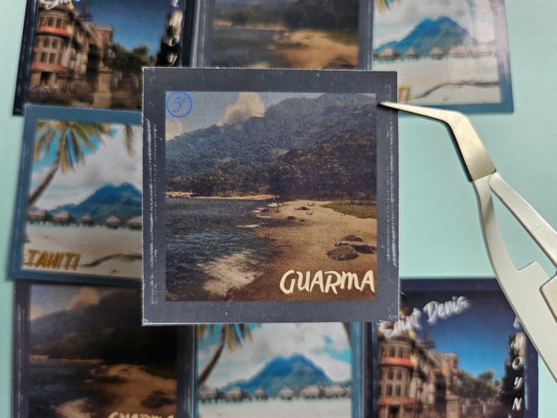May include: A vintage postcard with a photo of a beach scene. The postcard is blue and gray with the word "GUARDAMA" printed in white. The photo shows a beach with a body of water and mountains in the background.