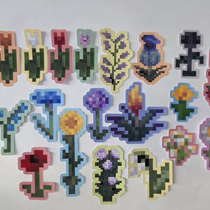 Peut inclure: Une collection d'autocollants de fleurs pixélisées de différentes couleurs, dont le rouge, le bleu, le jaune et le violet. Les autocollants présentent différents types et motifs de fleurs, avec une esthétique de jeu vidéo rétro.