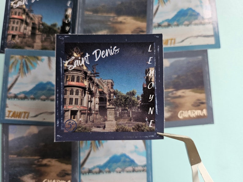 May include: A vintage-style postcard featuring a photo of a city street scene with buildings and a statue. The postcard is blue with white lettering that says "Saint Denis" and "LE MOYNE".