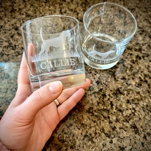 May include: Two clear glass tumblers with etched designs. The tumbler on the left has a dog silhouette and the name "Callie" etched on the front. The tumbler on the right has a dog silhouette and the name "Caleb" etched on the front.