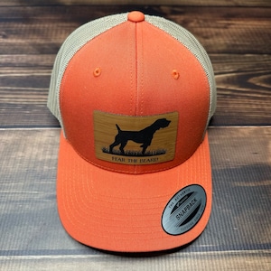 May include: Orange and tan trucker hat with a brown wood patch featuring a silhouette of a dog and the text "Fear the Beard".