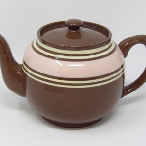 May include: A brown teapot with a pink and white striped design. The teapot has a round body and a curved handle.