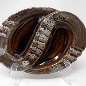 May include: A brown and white ceramic ashtray with a unique design. The ashtray has three separate compartments for cigarettes.