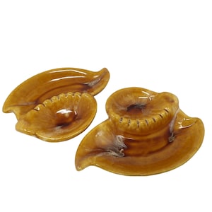 May include: Two brown ceramic ashtrays shaped like leaves with a small round depression in the center of each leaf.