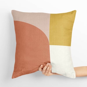 May include: A geometric patterned throw pillow with a peach, yellow, and white design. The pillow is made of a soft, textured fabric.