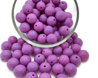May include: A large bowl filled with purple round beads. The beads are scattered on a white surface.