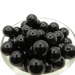 May include: A bowl filled with black round beads. The beads are smooth and shiny.