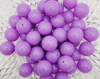 May include: A bowl filled with a large quantity of lavender purple round beads. The beads are smooth and shiny.