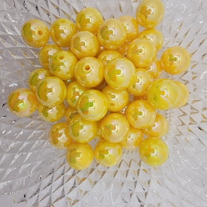 May include: A bowl of yellow iridescent beads with a flower design. The beads are approximately 1 inch in diameter.