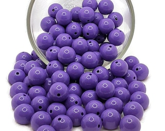 May include: A large quantity of purple round beads, some in a clear glass bowl, spilling out onto a white surface.