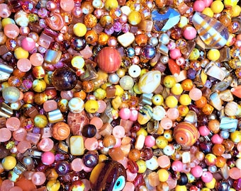 Puede incluir: Primer plano de una variedad de cuentas de vidrio de colores, incluyendo transparentes, rojas, naranjas, amarillas, verdes, azules, moradas y marrones. Las cuentas están dispuestas en un patrón aleatorio y son de diferentes tamaños y formas.