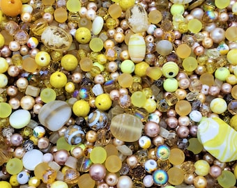 May include: A large assortment of yellow, brown, and white beads. The beads are made of glass, plastic, and wood. They are perfect for jewelry making, crafting, and home decor.