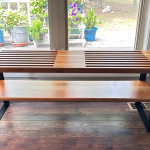 May include: A wooden bench with black metal legs and a slatted top. The bench has a lower shelf for storage.