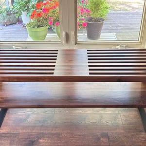 May include: A wooden bench with a slatted top and a lower shelf. The bench has black metal legs and is made of dark wood.
