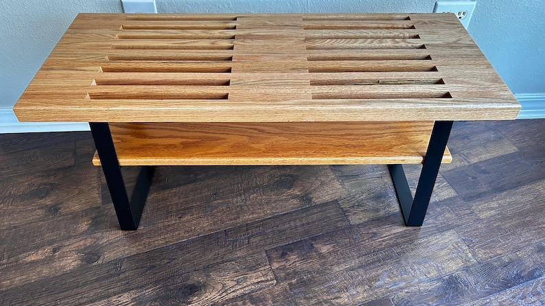 Puede incluir: Un banco de madera con una parte superior de listones y un estante inferior. El banco tiene patas de metal negro.