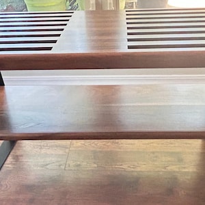 May include: A wooden coffee table with a dark brown finish. The tabletop features two sections with parallel slots. The table has a lower shelf and is supported by black metal legs. The table's dimensions are approximately 48 inches long, 24 inches wide, and 18 inches high.