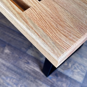 Puede incluir: Primer plano de una mesa de madera clara con acabado de veta de madera natural. La mesa tiene un borde biselado y est&aacute; sostenida por patas de metal negro.