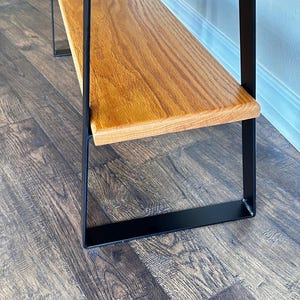 Puede incluir: Un banco de madera con una parte superior de listones y patas de metal negro. El banco tiene un estante inferior de madera.