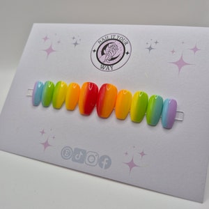 Può includere: Un set di dieci unghie finte color arcobaleno. Ogni unghia passa attraverso un colore diverso dell'arcobaleno, dal celeste al viola. Le unghie sono esposte su una carta bianca con la scritta "NAIL IT YOUR WAY".