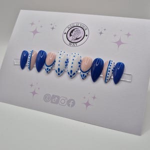 May include: A set of ten artificial nails in a variety of designs. The nails are in a range of colors, including navy blue, white, and a nude pink. Some nails feature a dotted pattern, while others have a solid color. The nails are displayed on a white card with the text "NAIL IT YOUR WAY".